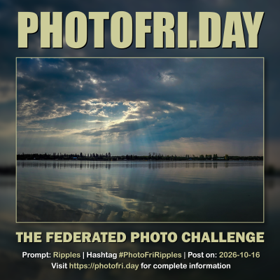 PhotoFri.day challenge card for Ripples, featuring sunlight breaking through dark clouds above a calm lake, reflected in rippled water. Text gives #PhotoFriRipples and the October 16, 2026 posting date.
